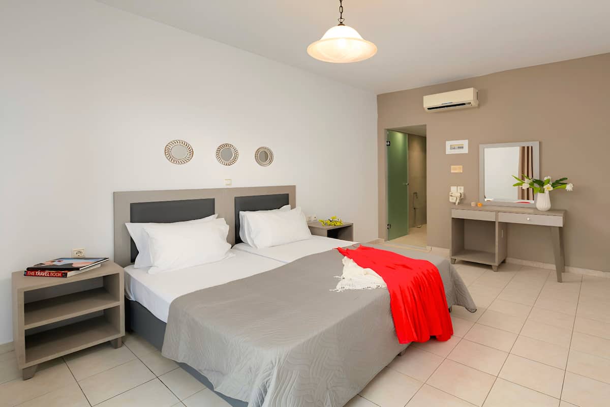 A modern hotel room with a bed, bedside tables, a vanity with a mirror, and an air conditioning unit.