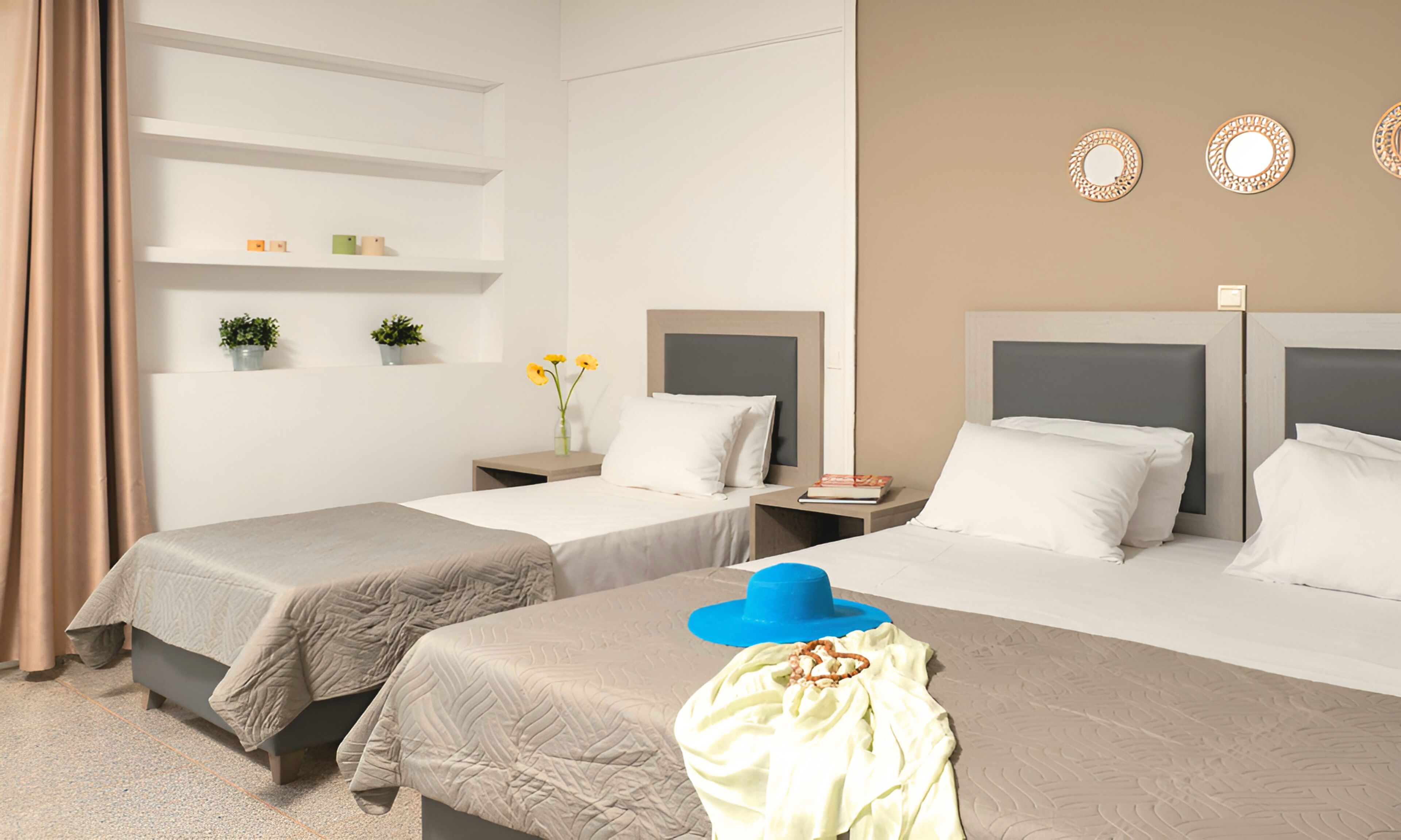 Habitación de hotel con dos camas, una mesita de noche, un espejo y una estantería con objetos decorativos.
