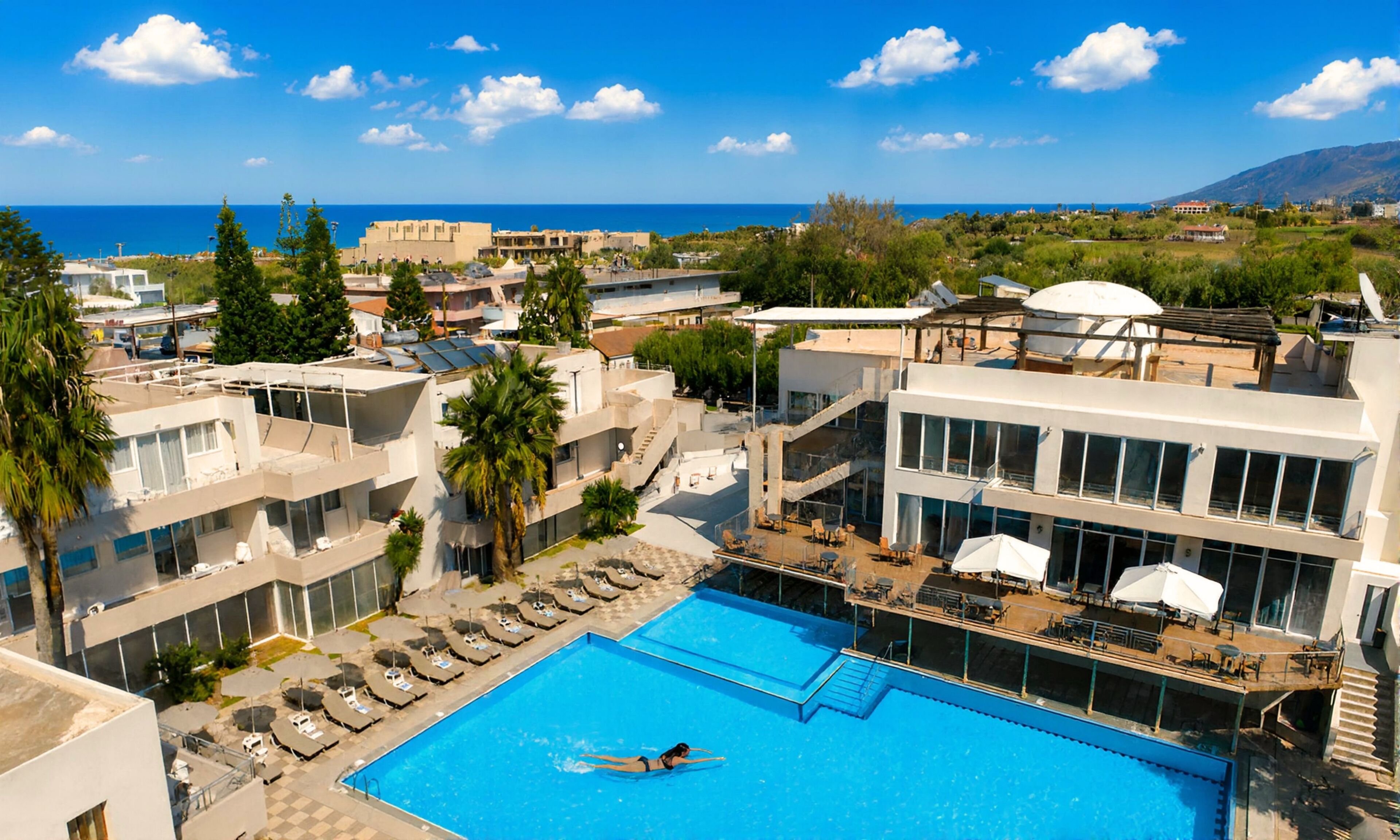 Una piscina sul tetto con vista sul mare, circondata da edifici e palme.