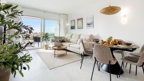A modern living room with a sofa, dining table, chairs, and a balcony with a view. - Brisa Azul 2-bedroom apartment in punta prima, pool, gym, jacuzzi (Torrevieja)