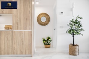 Ein modernes Interieur mit einem Holzschrank, einem runden Spiegel, einer Topfpflanze und einem Korb mit Blumen.
