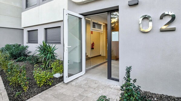 A modern building entrance with a glass door, number 02, and a small garden area with plants. - Brisa Azul 2-bedroom apartment in punta prima, pool, gym, jacuzzi (Torrevieja)