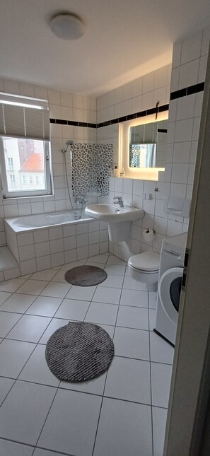 Un bagno con vasca, lavandino, water e lavatrice.