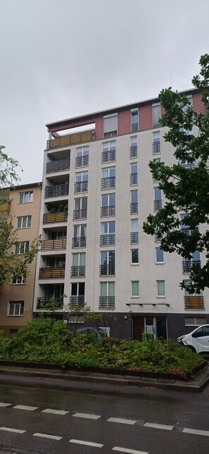 Un edificio residenziale a più piani con balconi, un'auto parcheggiata davanti e una strada in primo piano.