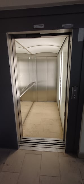 Un ascensor con paredes metálicas, un pasamanos y un cartel que indica que es un elevador.