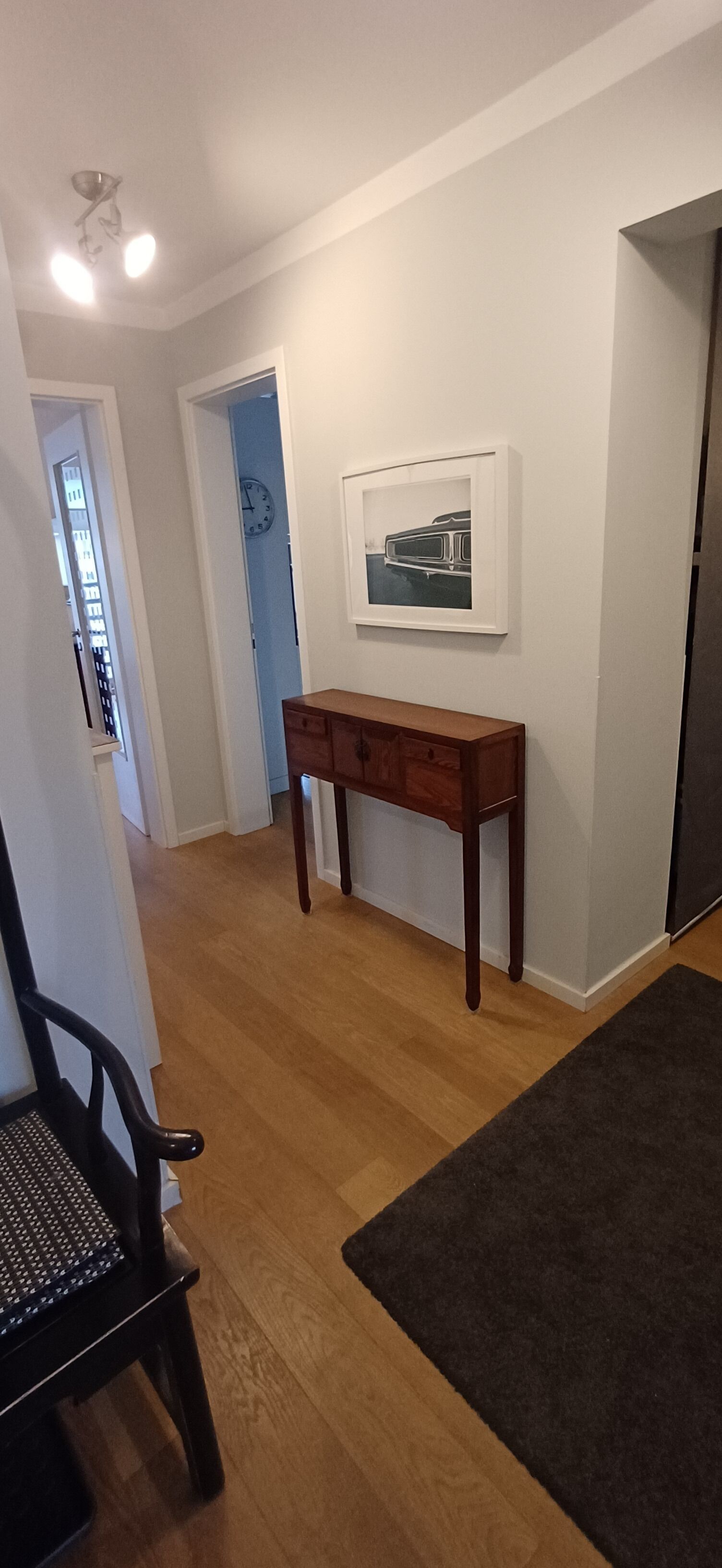 A hallway with a wooden bench, a dark rug, a wall clock, and a framed picture.