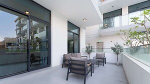 Een moderne buitenzitplaats met glazen balustrade, een potplant en uitzicht op de omliggende gebouwen.