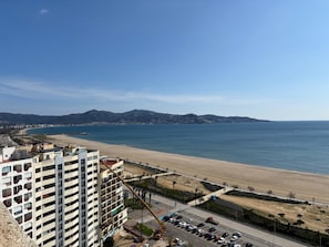 A coastal cityscape with a beach, a high-rise building, and a clear sky.