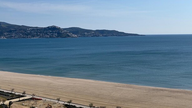 A coastal view with a sandy beach, a clear blue sea, and a distant mountain range. - Splendid apartment with sea view 50m from the beach with snack restaurant (Empuriabrava)