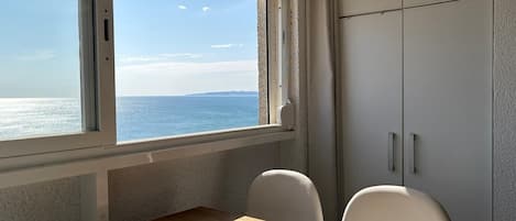 Una habitación con vista al mar, una mesa de madera, dos sillas y un armario blanco.