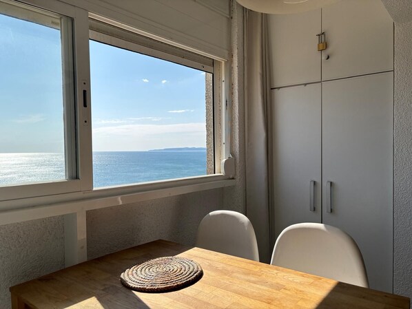 A room with a view of the sea, a wooden table, two chairs, and a white wardrobe.