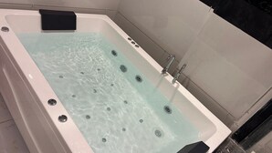 Eine rechteckige Badewanne mit klarem Wasser, einer schwarzen Bedienkonsole und einem Chrom-Wasserhahn.
