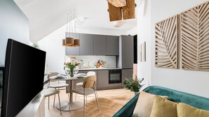 Uma cozinha moderna com armários cinza, uma área de jantar com mesa e cadeiras, um sofá verde-água e uma televisão de tela plana.