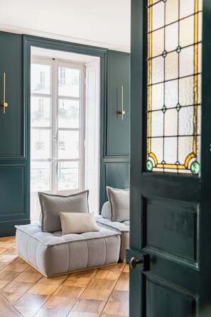 A room with a large window, a sofa with cushions, and a door with a stained glass design. - Set of 4 apartments l 240m2 l Sleeps 14 l Ideal for receptions (Grenoble)