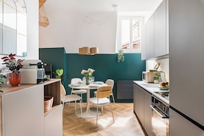 A modern kitchen with a dining area, wooden flooring, and a teal accent wall. - Set of 4 apartments l 240m2 l Sleeps 14 l Ideal for receptions (Grenoble)