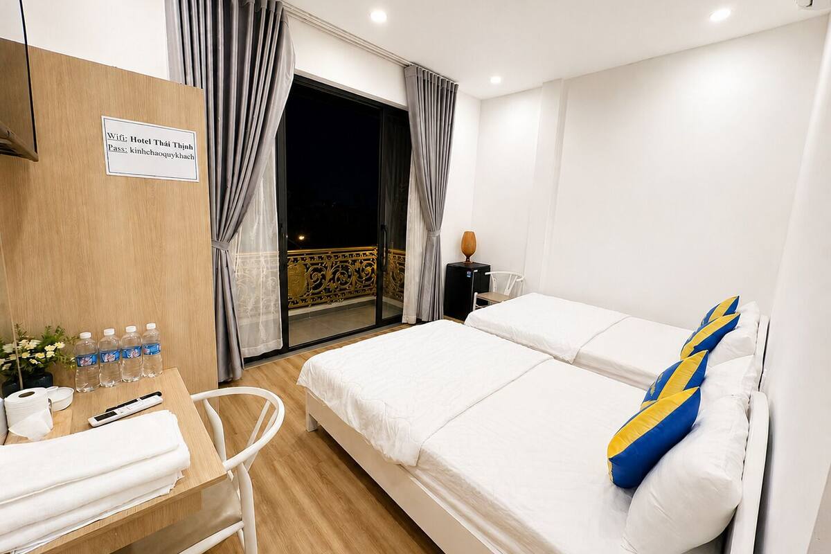 A hotel room with a bed, a desk with toiletries, a chair, and a balcony with a view.