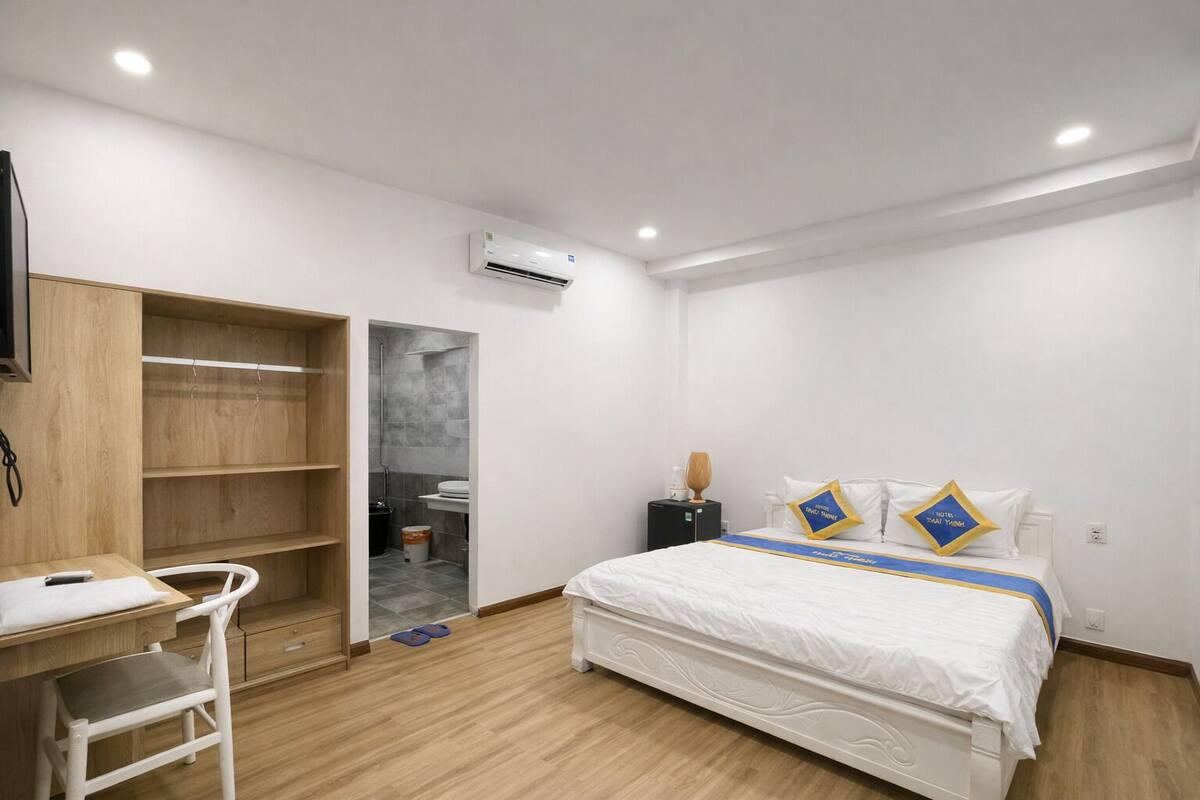 A hotel room with a bed, a desk, a chair, a wardrobe, and an air conditioning unit.