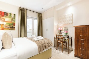 Un dormitorio con cama, escritorio, armario y ventana con cortinas.