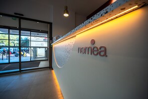 A reception desk with a sign that reads 'nomea' and a glass door entrance. - Nemea Appart Hotel Nice Sunset Arenas (Nice)