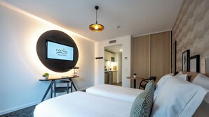 Habitación de hotel con cama, escritorio, silla, televisión redonda montada en la pared y una planta pequeña en maceta.