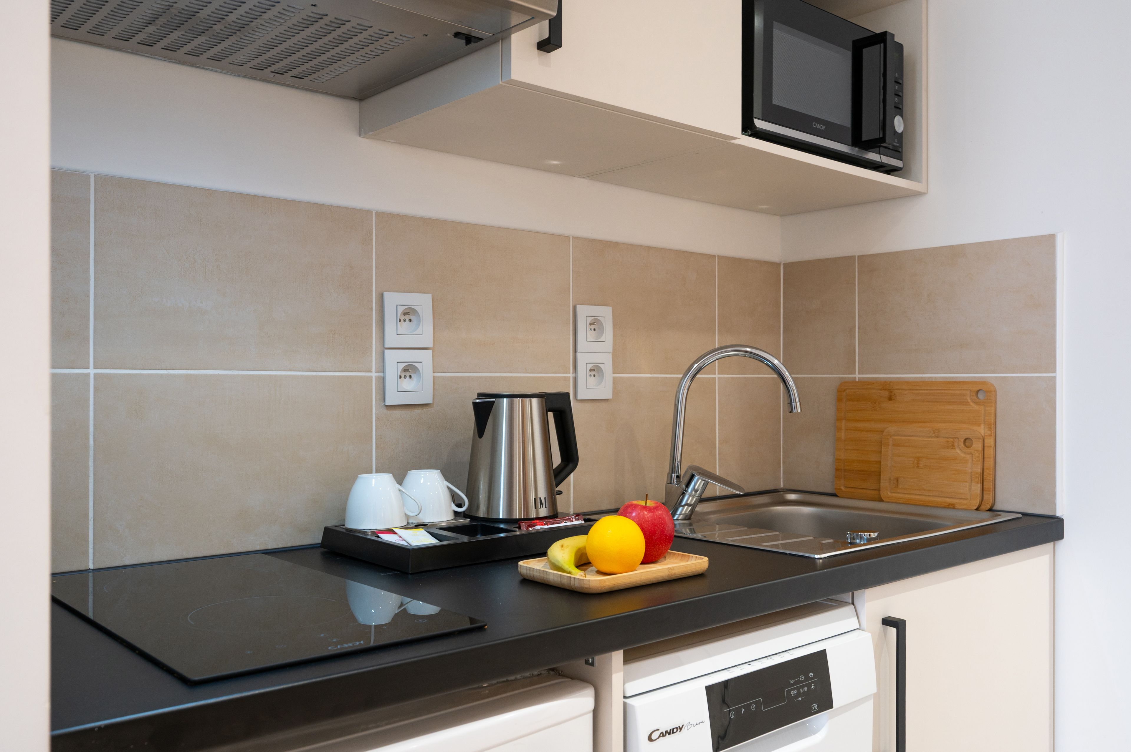 A modern kitchen with a black countertop, stainless steel appliances, a microwave above the sink, and a wooden cutting board with fruit.