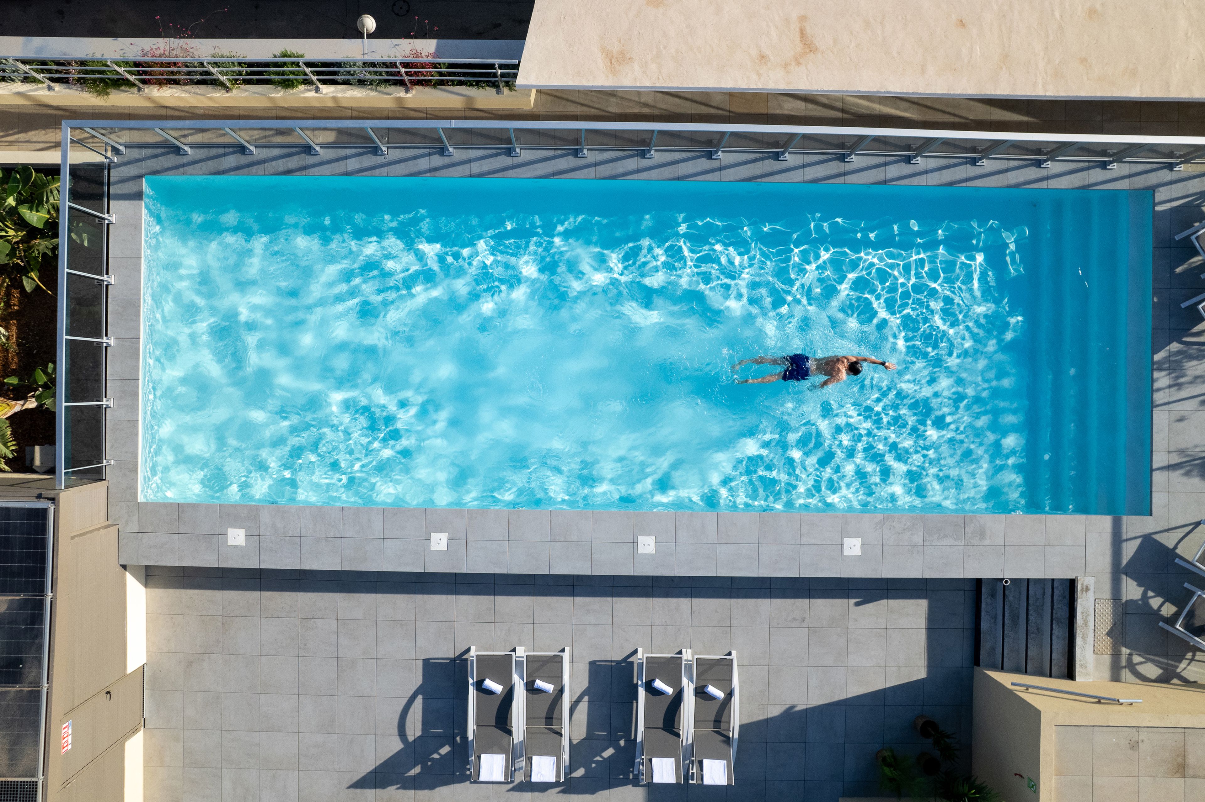 Una piscina elevada con una persona nadando, rodeada de sillas de descanso y un suelo de baldosas.