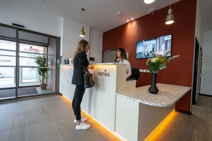 A reception desk with a 'nemea' sign, a potted plant, and a framed picture on the wall. - Nemea Appart Hotel Nice Sunset Arenas (Nice)