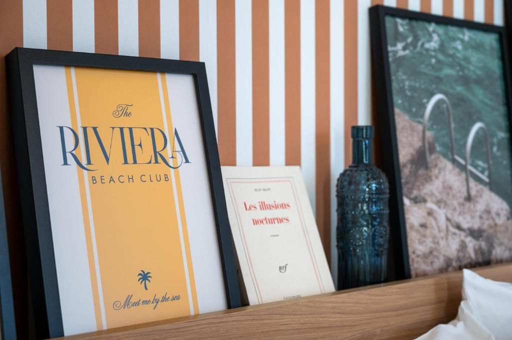 Un cartello incorniciato per 'The Riviera Beach Club' con il logo di una palma, un libro rilegato dal titolo 'Les illusions nocturnes' e una bottiglia decorativa.