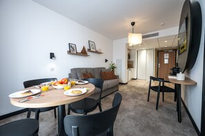 A modern dining area with a round table, chairs, and a sofa in the background. - Nemea Appart Hotel Nice Sunset Arenas (Nice)