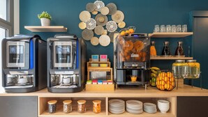 Una estación de café con varias máquinas de café, una cesta de fruta y una variedad de condimentos.
