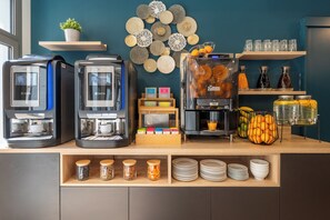 Un espace dédié au café, équipé de plusieurs machines à café, d’un panier de fruits et d’une variété de condiments.