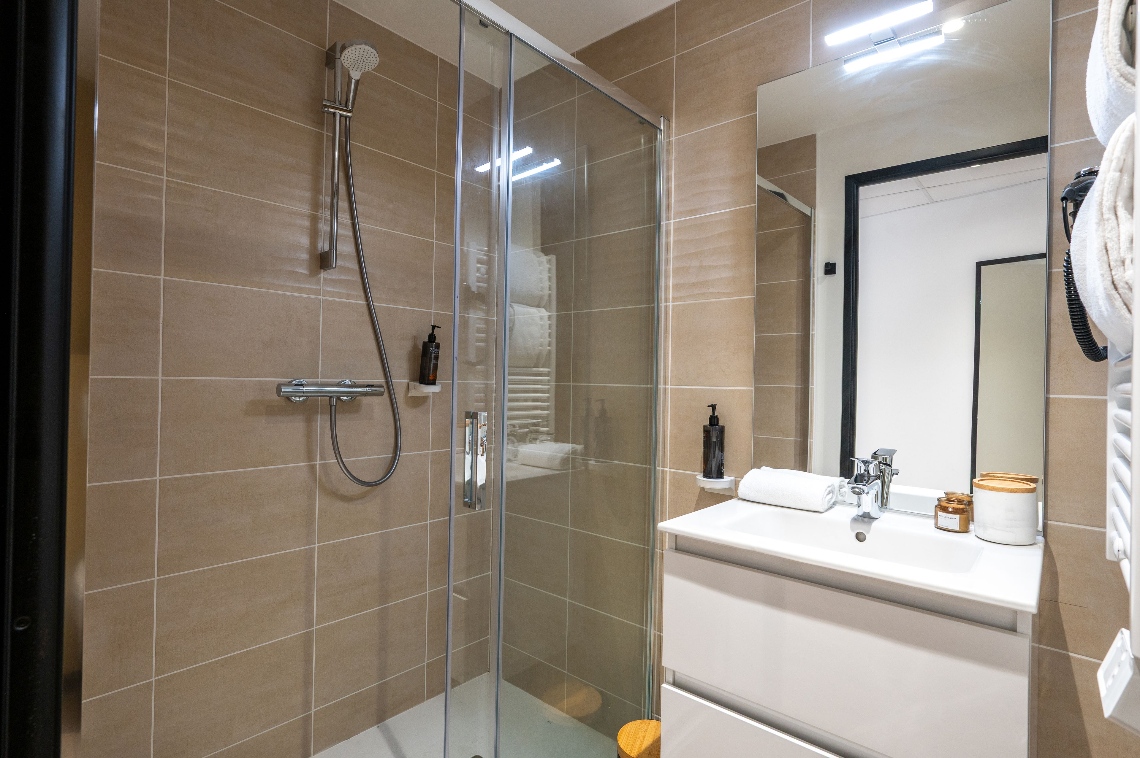 Un baño moderno con cabina de ducha de vidrio, un lavabo blanco con espejo y un perchero para toallas.