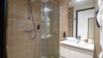 Un baño moderno con cabina de ducha de vidrio, un lavabo blanco con espejo y un perchero para toallas.