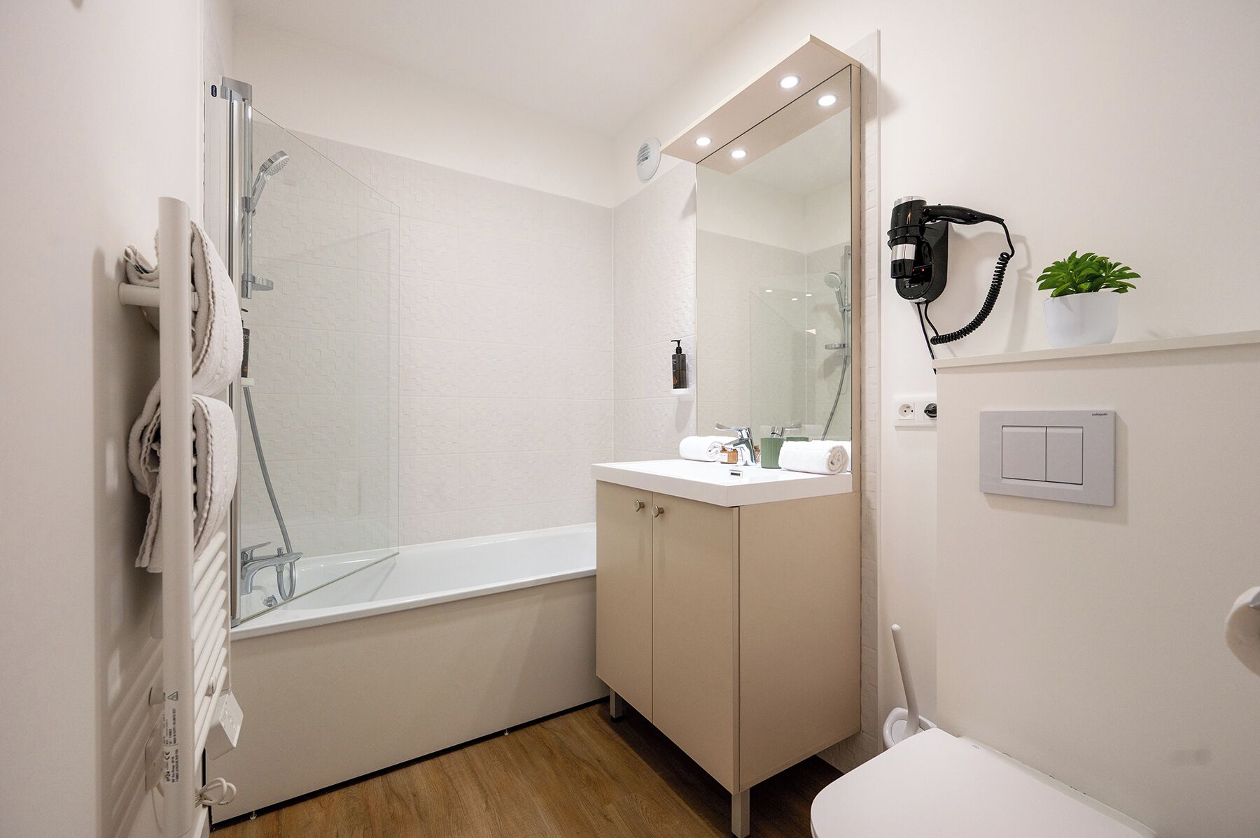 Et moderne badeværelse med et glasbadeværelsesafskærmning, en hvid vask med spejl og et toilet.