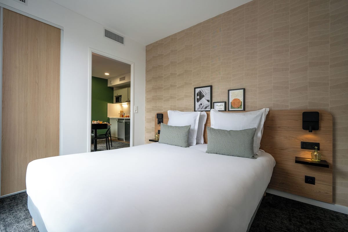 Quarto de hotel moderno com uma cama grande, duas mesas de cabeceira com abajures, uma cabeceira de madeira e uma parede verde.