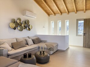 A modern living room with a sectional sofa, decorative wall art, a ceiling fan, and large windows. - Elegant Corfu Villa with Private Pool & Sea Views (Corfu)
