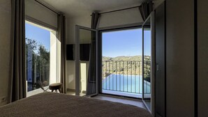 Un dormitorio con una cama grande, una silla y un ventanal corredero que da a un balcón con vista a la piscina.