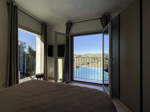 A bedroom with a large bed, a chair, and a sliding glass door leading to a balcony with a pool view. - Elegant Corfu Villa with Private Pool & Sea Views (Corfu)