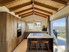 A modern kitchen with wooden beams, a large window, and a view of the landscape. - Elegant Corfu Villa with Private Pool & Sea Views (Corfu)