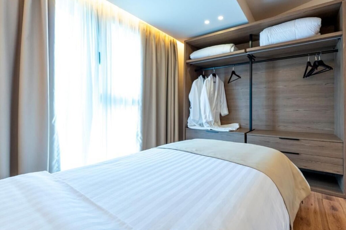 Una habitación de hotel con una cama, un armario con ropa colgada y una ventana con cortinas.