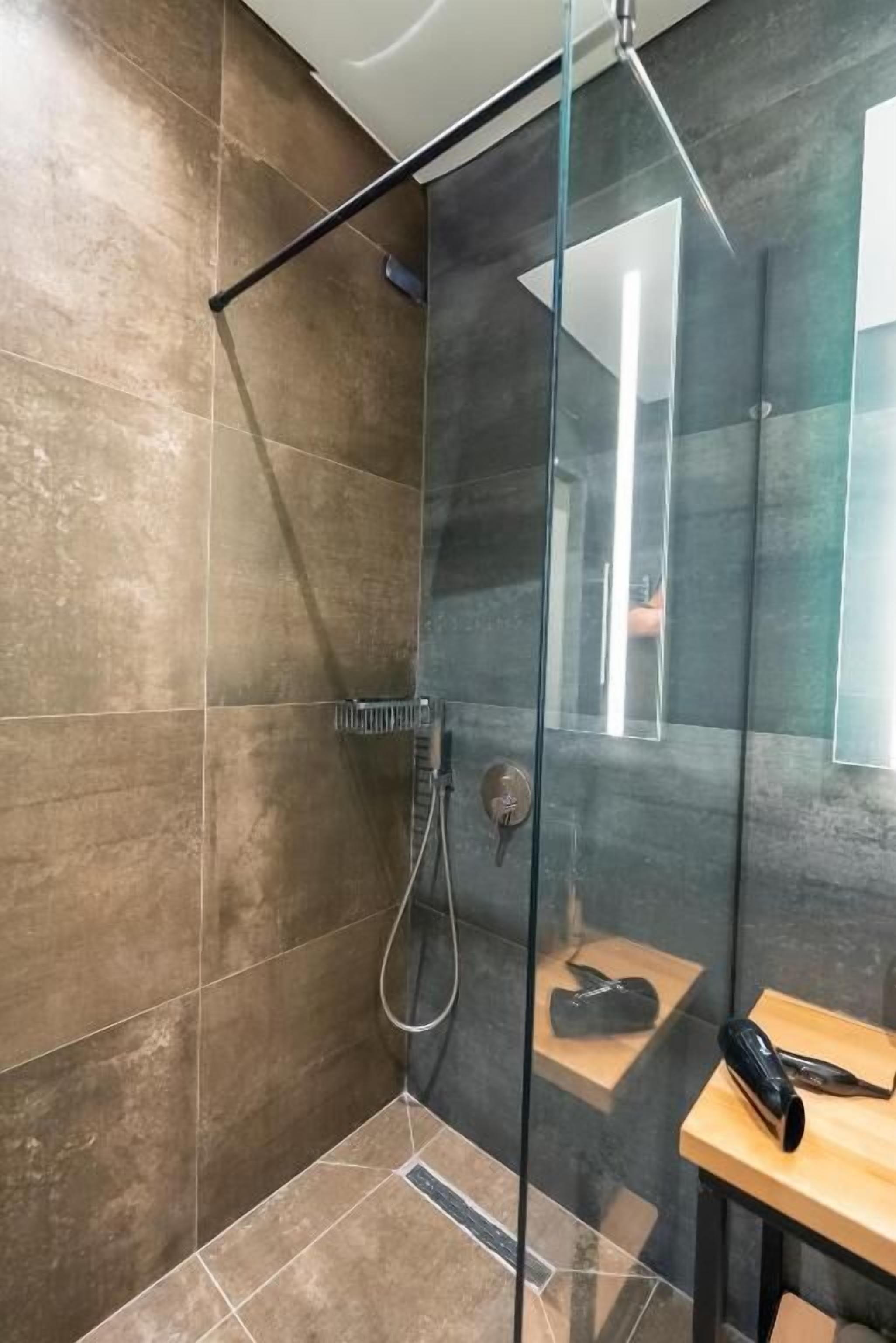 Un baño moderno con ducha de vidrio, una mesita de madera y un perchero para toallas.