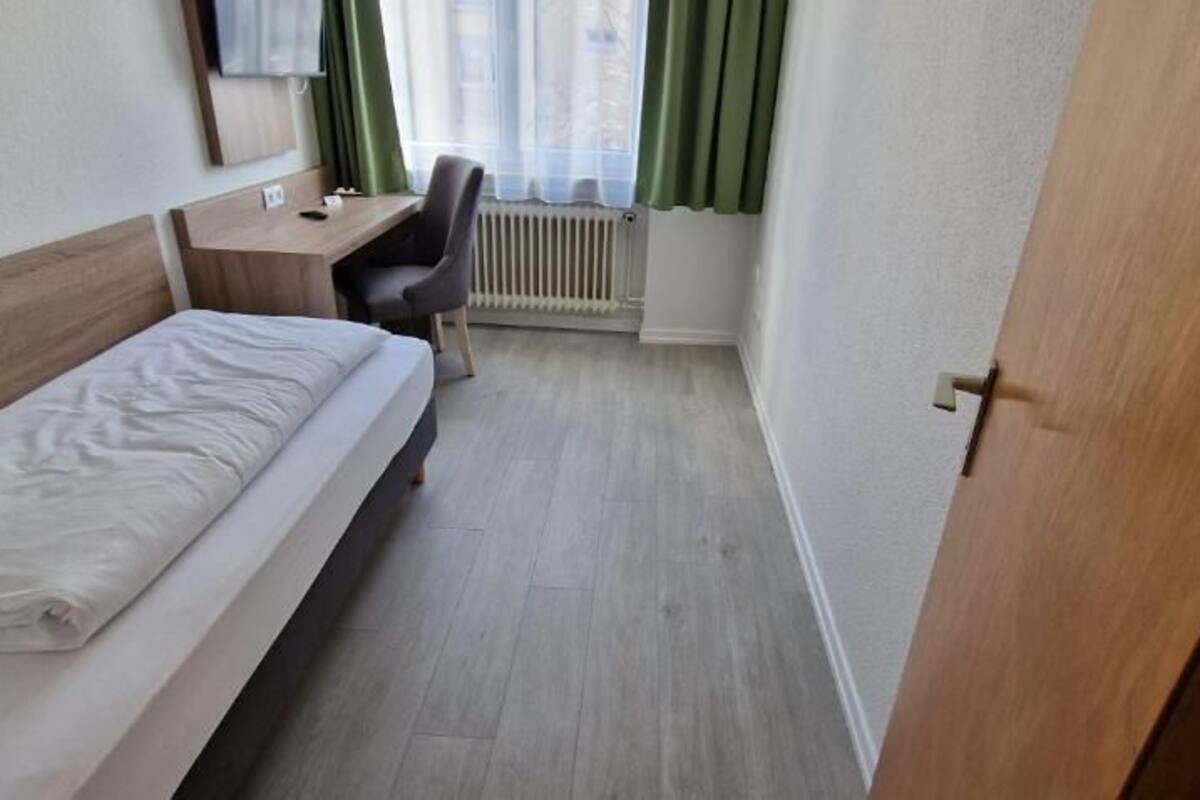 Una habitación de hotel pequeña con una cama individual, un escritorio, una silla y un radiador.