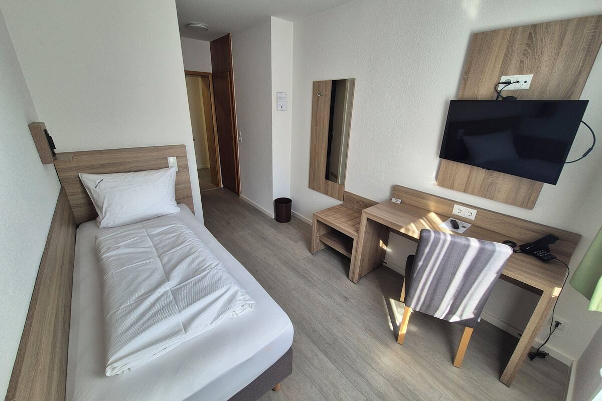 Habitación de hotel con cama, escritorio, silla, televisión y espejo.