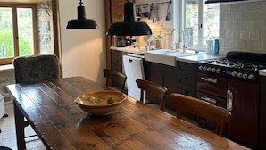 Une cuisine avec une table en bois, des chaises, un fourneau et des luminaires suspendus.