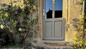Un bâtiment en pierre avec une porte en bois, des marches menant à l’entrée et de la verdure tout autour.
