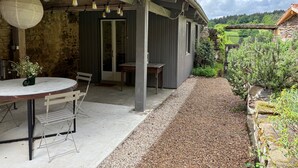 Une terrasse couverte avec une table et des chaises, un mur en pierre et une vue sur un paysage verdoyant.