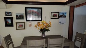 Un coin repas avec une table et des chaises en bois, des tableaux encadrés au mur et un vase rempli de fleurs.