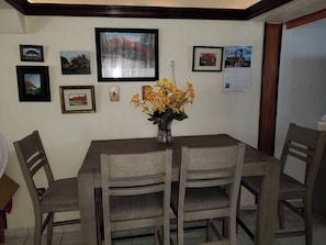 A dining area with a wooden table and chairs, framed pictures on the wall, and a vase with flowers. - Charming 3-bedroom House Steps From Luquillo Beach (Luquillo)