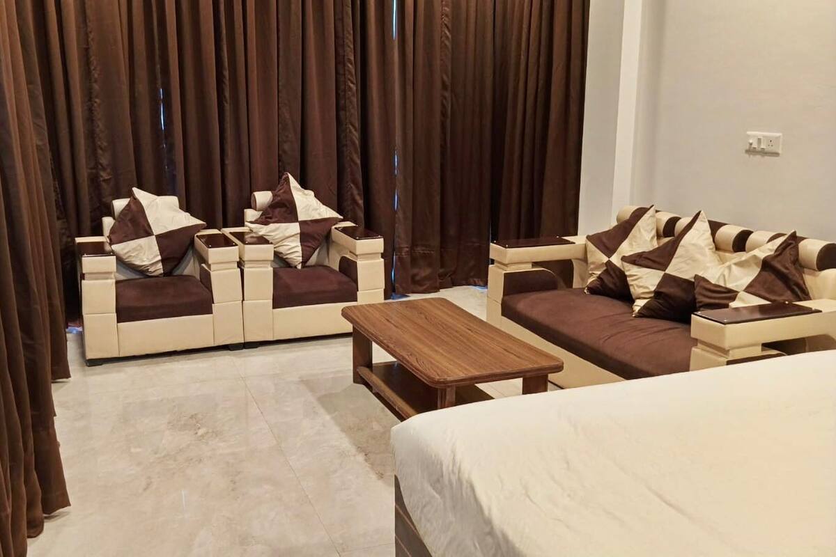 Quarto de hotel com cama, dois sofás, mesa de centro de madeira e um painel de cortinas.