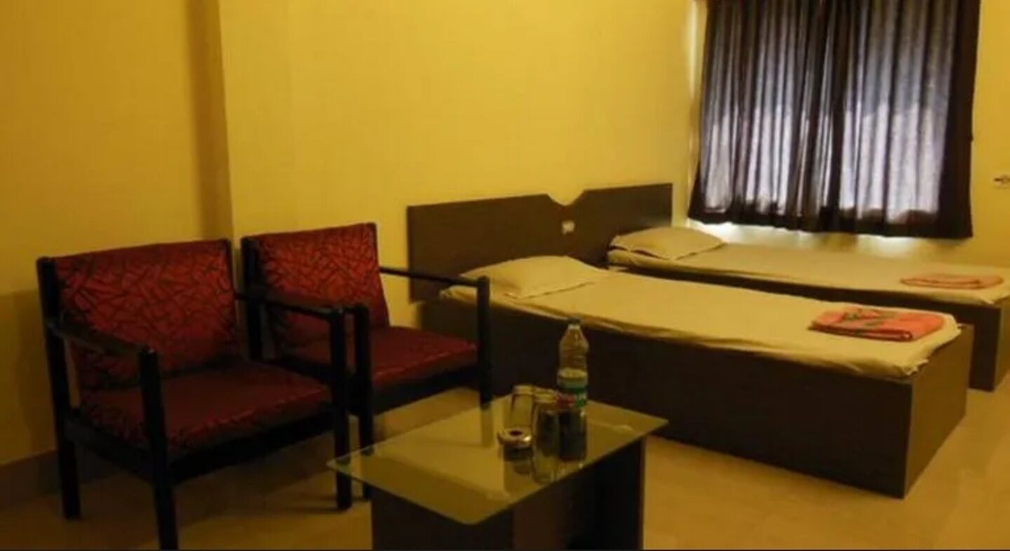 Una habitación de hotel con una cama individual, una silla, una mesita y una ventana con cortinas.